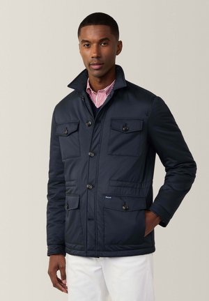 Chaqueta acolchada azul marino con cuatro bolsillos frontales, cierres de botones y un cuello alto. Textura suave y ajuste entallado.