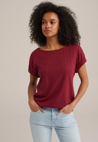 Burgundia lühikeste varrukatega pluus, millel on kalasaba tekstuur, koos laia kaeluse ja keerdvarrukatega, kombineeritud heleda sinise teksapükstega.