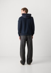 Navy sweatshirt with a padded hood, ribbed cuffs, and hem; paired with loose, dark gray jeans featuring back pockets and a straight leg.
