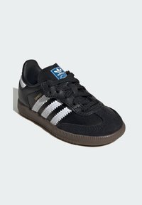 Crne Adidas Samba tenisice od kombinacije antilopa i kože, s tri bijele pruge, podstavljenim ovratnikom i smešim gumenim potplatom.