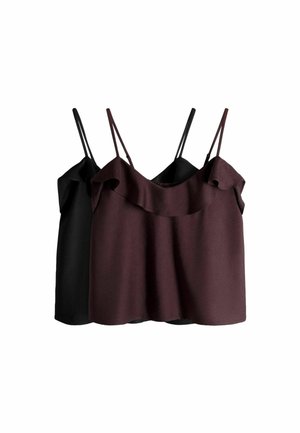 Ung kvinde iført en mørklilla ærmeløs top og lyse denimshorts, der står udendørs nær stentrin og græs.