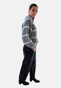 Grijze gebreide trui met witte strepen, cropped ontwerp en brede mouwen, gecombineerd met hoge zwarte jeans en zwarte enkellaarsjes.