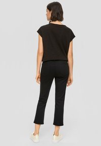 Zwarte cropped jeans met een slank ontwerp en achterzakken, gecombineerd met een losse zwarte top met korte mouwen van textuurstof.