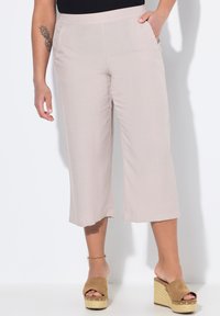 Světlé béžové kalhoty culotte vyrobené z měkkého materiálu, s širokým střihem a postranními kapsami. Kombinované s hnědými platformovými sandálemi.