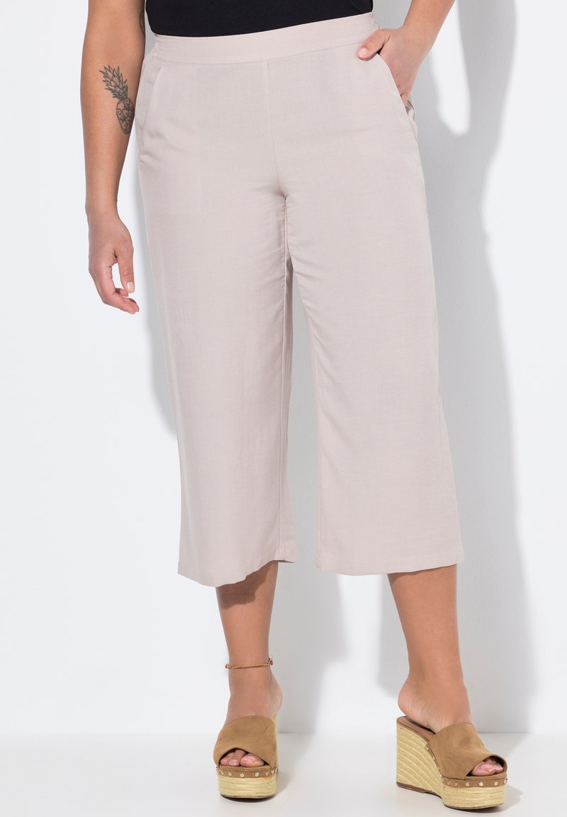 Světlé béžové kalhoty culotte vyrobené z měkkého materiálu, s širokým střihem a postranními kapsami. Kombinované s hnědými platformovými sandálemi.