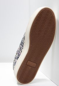 Vit sneaker med en texturerad övre del i ett blommönster. Gummisul med zickzack-mönster och "NO NAME" präglat på hälen.