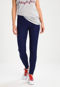 Leggings blu navy con un design aderente, realizzati in un tessuto elasticizzato. Abbinati a un top grigio e sneakers bianche con lacci rossi.