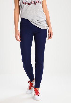 Navy leggings with a fitted design, made from a stretchy fabric. Paired with a gray tank top and white sneakers with red laces.
