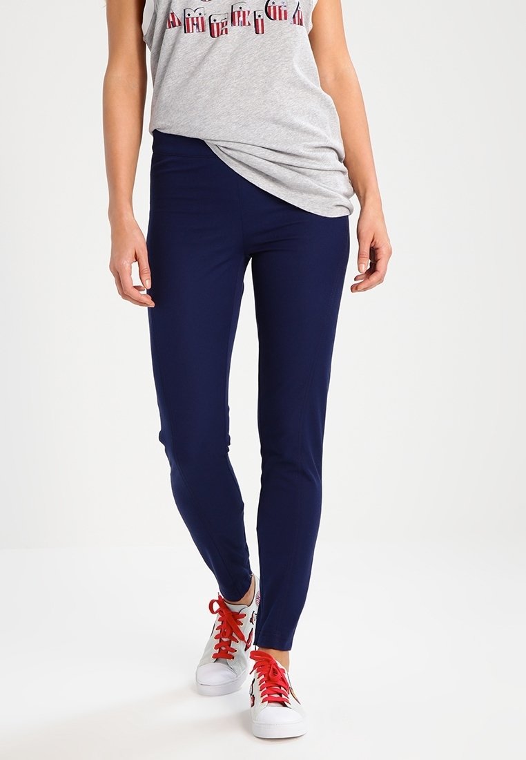 Leggings blu navy con un design aderente, realizzati in un tessuto elasticizzato. Abbinati a un top grigio e sneakers bianche con lacci rossi.