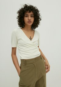 Witte geribbelde top met korte mouwen en een diepe V-hals, gecombineerd met olives groene hoge taille broek. Eenvoudig ontwerp en gladde textuur.