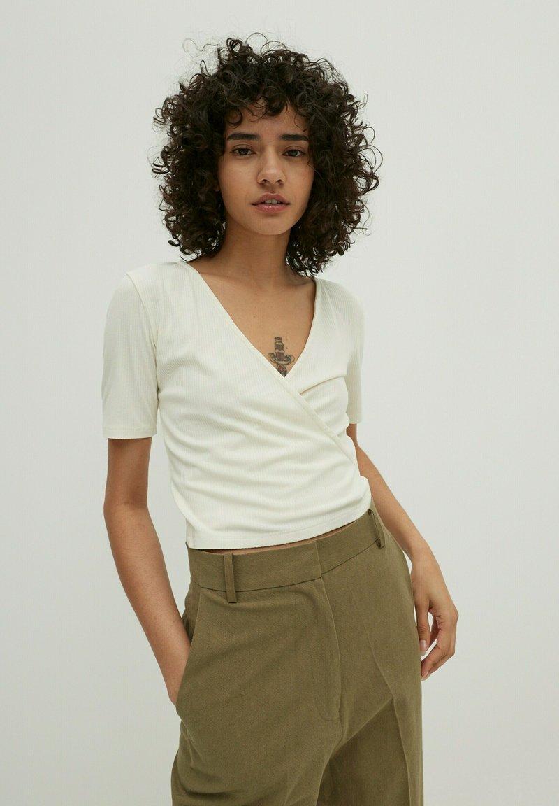 Witte geribbelde top met korte mouwen en een diepe V-hals, gecombineerd met olives groene hoge taille broek. Eenvoudig ontwerp en gladde textuur.