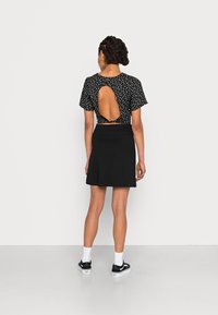 Crop top noir à motif floral avec découpe dans le dos, associé à une jupe noire évasée. Le mannequin porte des baskets noires et des chaussettes blanches.