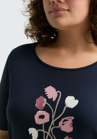 Haut bleu marine avec un imprimé floral en rose et blanc. Encolure arrondie et manches courtes, fabriqué en tissu doux et lisse.