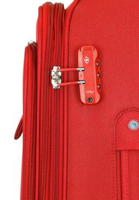 Maleta roja con un exterior de tela texturizada, múltiples cremalleras y un candado aprobado por la TSA, con una base roja y botones negros.