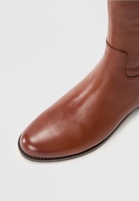 Brown leather ankle boot with a smooth finish, rounded toe, and subtle stitching detail along the side and opening. Minimalist design.