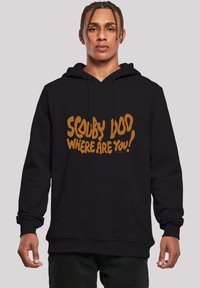 Sudadera negra con bolsillo frontal, con un atrevido texto naranja: "¡SCOOBY DOO, ¿DÓNDE ESTÁS!" El texto tiene una fuente lúdica e irregular.