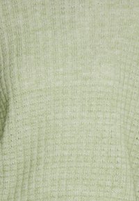 Ljusgrön texturerad tyg med ett subtilt ribbat mönster. Mjukt, stickat material med en lätt glans och upphöjda trådar.