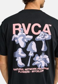 Black cotton t-shirt with a graphic print featuring light purple mushrooms and pink text stating "RVCA" and "NATURAL NETWORK PROGRAM FLOWERS - MYCELIUM."