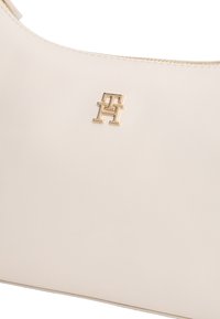 Τσάντα χειρός από λείο δέρμα σε κρεμ απόχρωση με χρυσλό διακριτικό λογότυπο "TH" και λεπτομέρεια χρυσλού φερμουάρ στην κορυφή.
