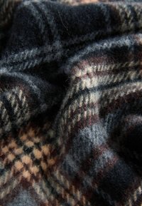Țesătură din lână cu un model tartan ce include culori albastre închise, bej și maro. Textură moale cu fibre vizibile și pliuri suprapuse.