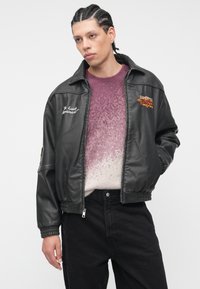 Melna ādas bombera jaka ar elastīgiem aprocēm un rāvējslēdzēju. Rotāta ar izšūtu tekstu un krāsainām uzlīmēm. Valkāta virs gradienta violetas džemperis.