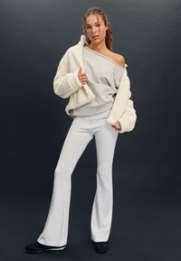 Sivka pletena džemper in ujemajoče se razširjene hlače, v kombinaciji s smetano teksturiranim jopičem. Obleka ponuja sproščen kroj in mehke materiale.