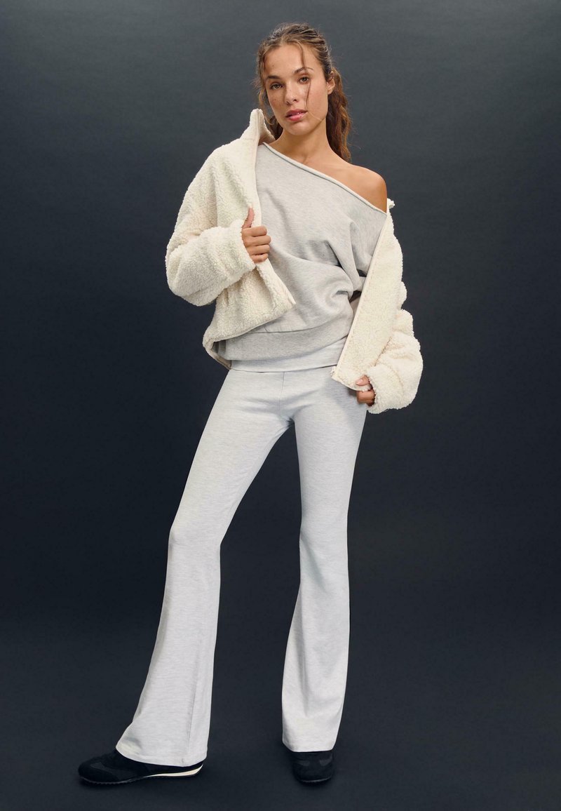 Sivka pletena džemper in ujemajoče se razširjene hlače, v kombinaciji s smetano teksturiranim jopičem. Obleka ponuja sproščen kroj in mehke materiale.