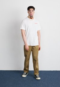 White short-sleeve t-shirt featuring red "CONVERSE" text, paired with khaki pants and black canvas sneakers with white soles.