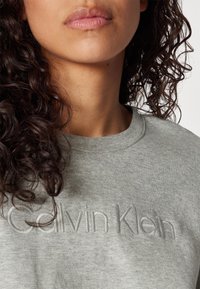 Světle šedá mikina s výšivkou loga "Calvin Klein", s kulatým výstřihem a měkkou texturovanou tkaninou.