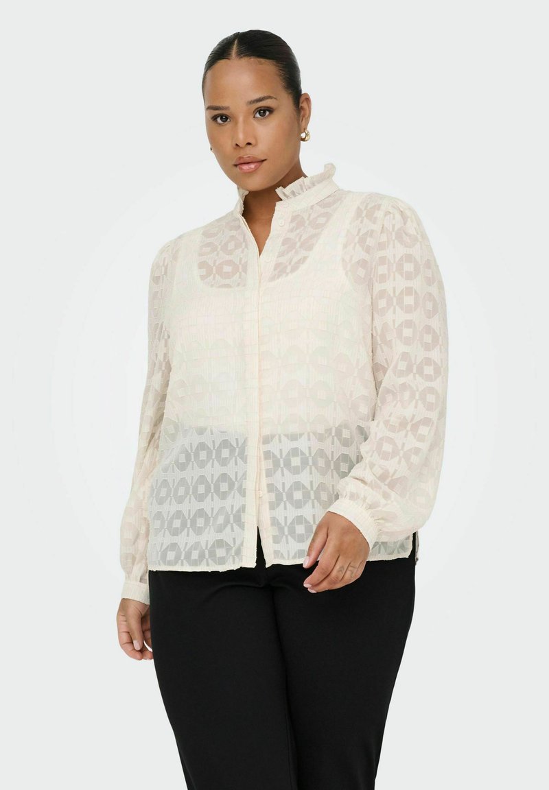 Blusa leggera e trasparente color crema con motivi geometrici, colletto alto e chiusura con bottoni. Maniche lunghe con polsini arricciati.