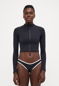 Black cropped long-sleeve top with a front zipper and high neckline, paired with black bikini bottoms featuring white accents. Smooth texture.
