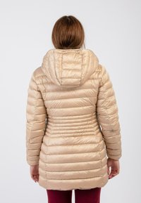 Beige pufferjack met een capuchon, voorzien van een gewatteerd ontwerp, geribbelde textuur en een getailleerd silhouet, dat tot halverwege de dijen reikt.