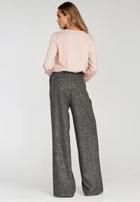 Jasnoróżowa bluzka z długim rękawem w połączeniu z szerokimi spodniami w szary wzór. Stylizacja charakteryzuje się luźnym krojem i gładką teksturą.