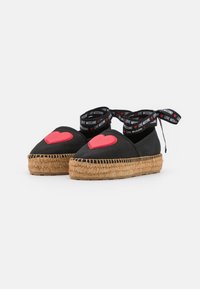 Black platform espadrilles with red heart patches on toes and black ankle ribbons printed with "LOVE MOSCHINO" and red hearts.