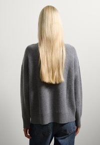 Grauer gerippter Strickpullover mit fallenden Schultern, getragen über blauen Jeans, zeigt eine lässige Passform und weiche Textur, von hinten gesehen.