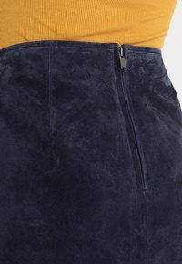 Marinblå mockaskirt med en mjuk textur, bakdragkedja och en figurnära design, kombinerad med en ribbad topp i senapsgul.