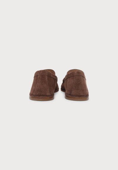 Paire de mocassins en daim marron à enfiler, vue de dos sur un fond clair uni.