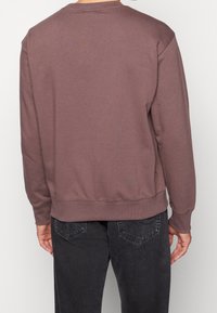 Vinröd sweatshirt med rund halsringning, ribbade muddar och fåll. Bakifrån visar den en slät yta utan synliga mönster eller detaljer.