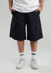 Shorts cargo noirs avec deux poches latérales et une poche à rabat. Fabriqués en tissu résistant, avec une coupe droite et une longueur jusqu'aux genoux.