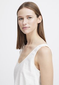 Weißes Leinen-Top mit breiten Schulterträgern und rundem Ausschnitt, das eine weiche Textur und ein minimalistisches Design aufweist.