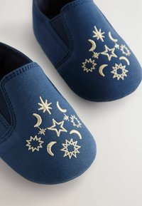 Chaussures slip-on bleu marine en tissu, ornées de broderies dorées de étoiles et de lunes, avec des panneaux latéraux élastiques pour un enfilage facile.