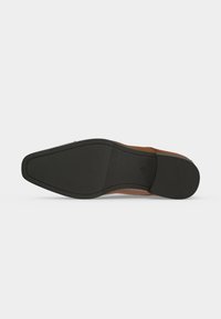 Semelle d'une chaussure habillée en cuir marron montrant une semelle inférieure en caoutchouc noir texturé avec des coutures autour des bords sur fond blanc.
