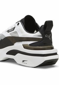 Sneaker Puma in bianco e nero con tomaia in rete testurizzata, accenti trasparenti e suola ammortizzata. Presenta il logo e un design minimalista.