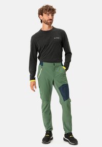 Groene outdoorbroeken met navy accenten, ritszakken en een getailleerd ontwerp. Draag ze met een zwart longsleeve shirt en zwarte schoenen.