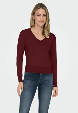 Maglione bordeaux a V con maniche lunghe, texture a maglia e orlo a coste, abbinato a jeans blu. Design semplice e classico.