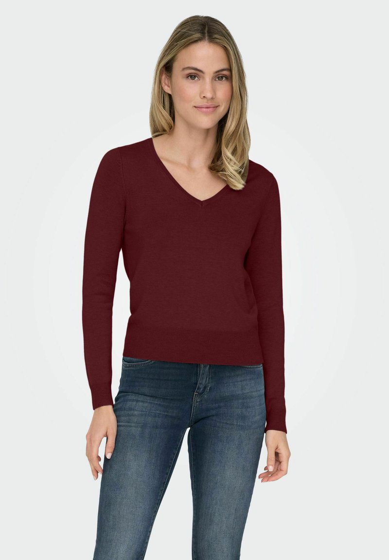Maglione bordeaux a V con maniche lunghe, texture a maglia e orlo a coste, abbinato a jeans blu. Design semplice e classico.