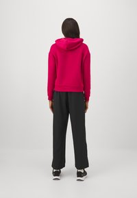 Fuksia huppari, rento malli, ribbireunukset, yhdistetty mustiin leveisiin housuihin, esitetty takaa.