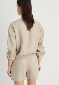 Beige linne-topp med rullade ärmar i kombination med matchande shorts. Avslappnad passform, synliga sömmar och resårmidja på shortsen.