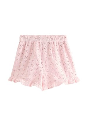 Smilende pige med sort hår i en hvid T-shirt med korte ærmer, pink øjlynlige shorts, pink sokker og grå sneakers står med hånden på hoften.