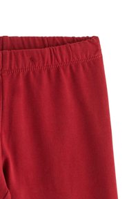Røde, bløde leggings i stof med en elastisk linning, der har en glat tekstur og ingen synlige mønstre. Sømmen har synlige sømkantdetaljer.